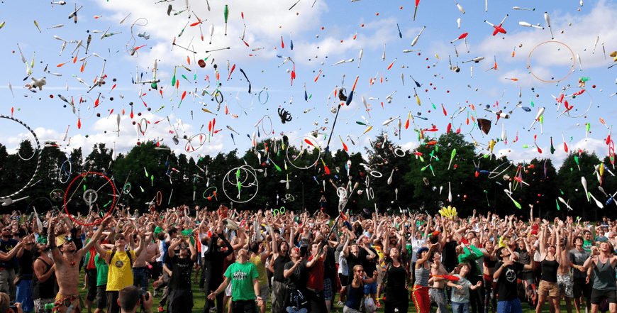 crowd throwing juggling equipment in the air in outdoor space