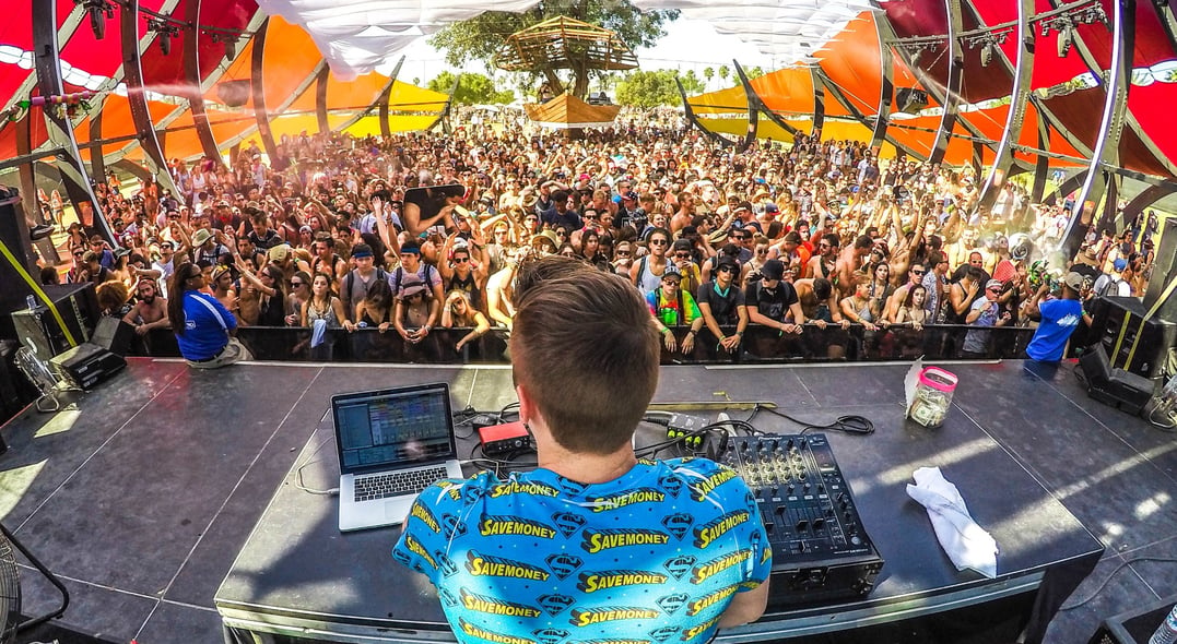 DJ playing decks on stage in front of a crowd at a music festival