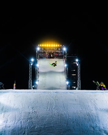 a snowboarder doing a jump at night time with people taking photos