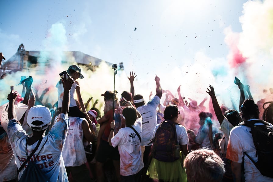 crowd holding phones, facing a stage, covered in powdered colourful powder that is being thrown around. Fa