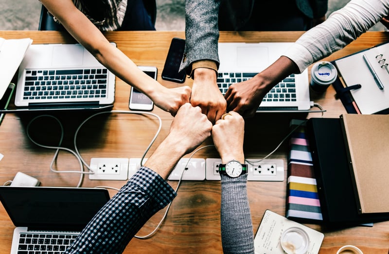 group of hands in middle over table with laptops and phones