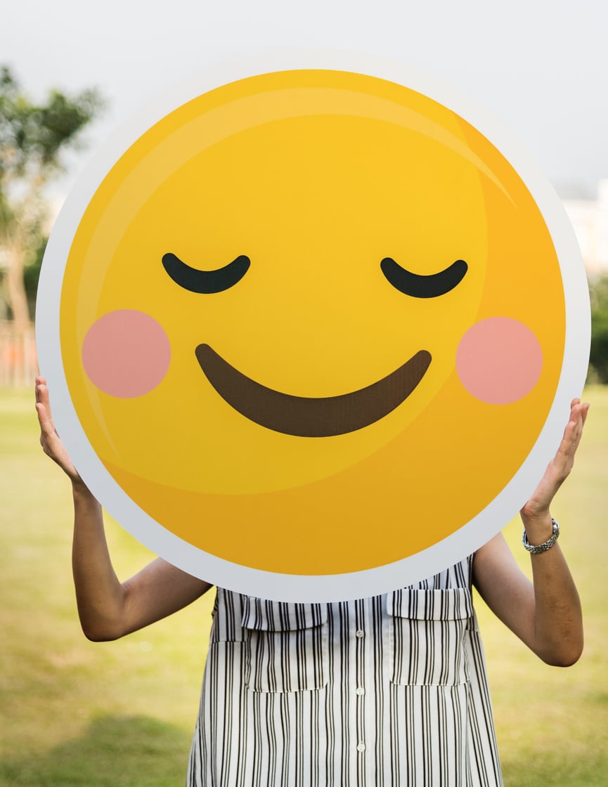 woman holding big cut out image of a smiley face emoticon